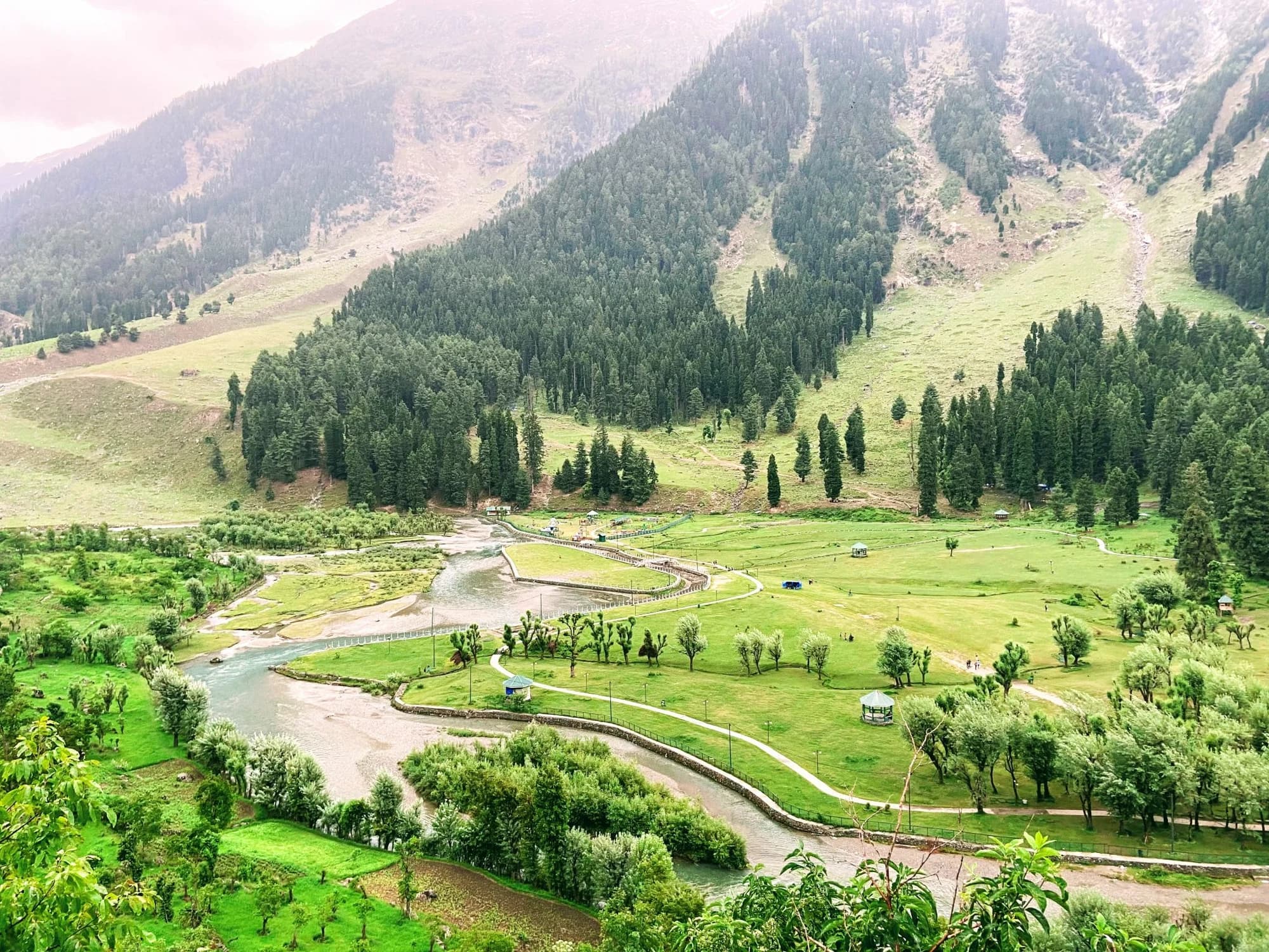 A winding river and green meadows beneath pine-covered mountains in Betaab Valley, Pahalgam